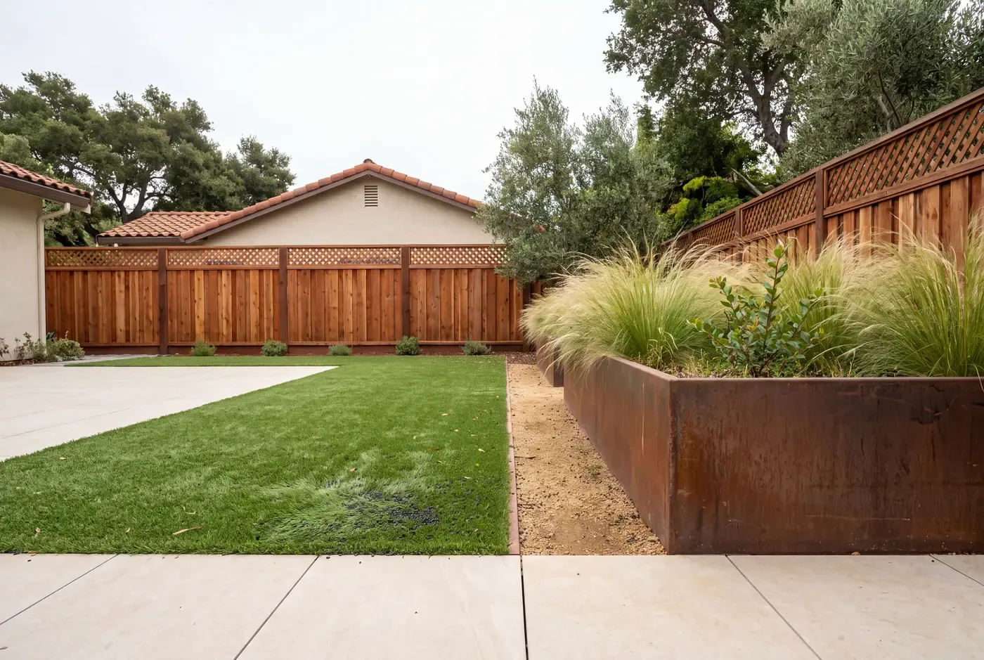 Close-up of synthetic turf blades and dark rubber infill granules adjacent to a concrete patio edge