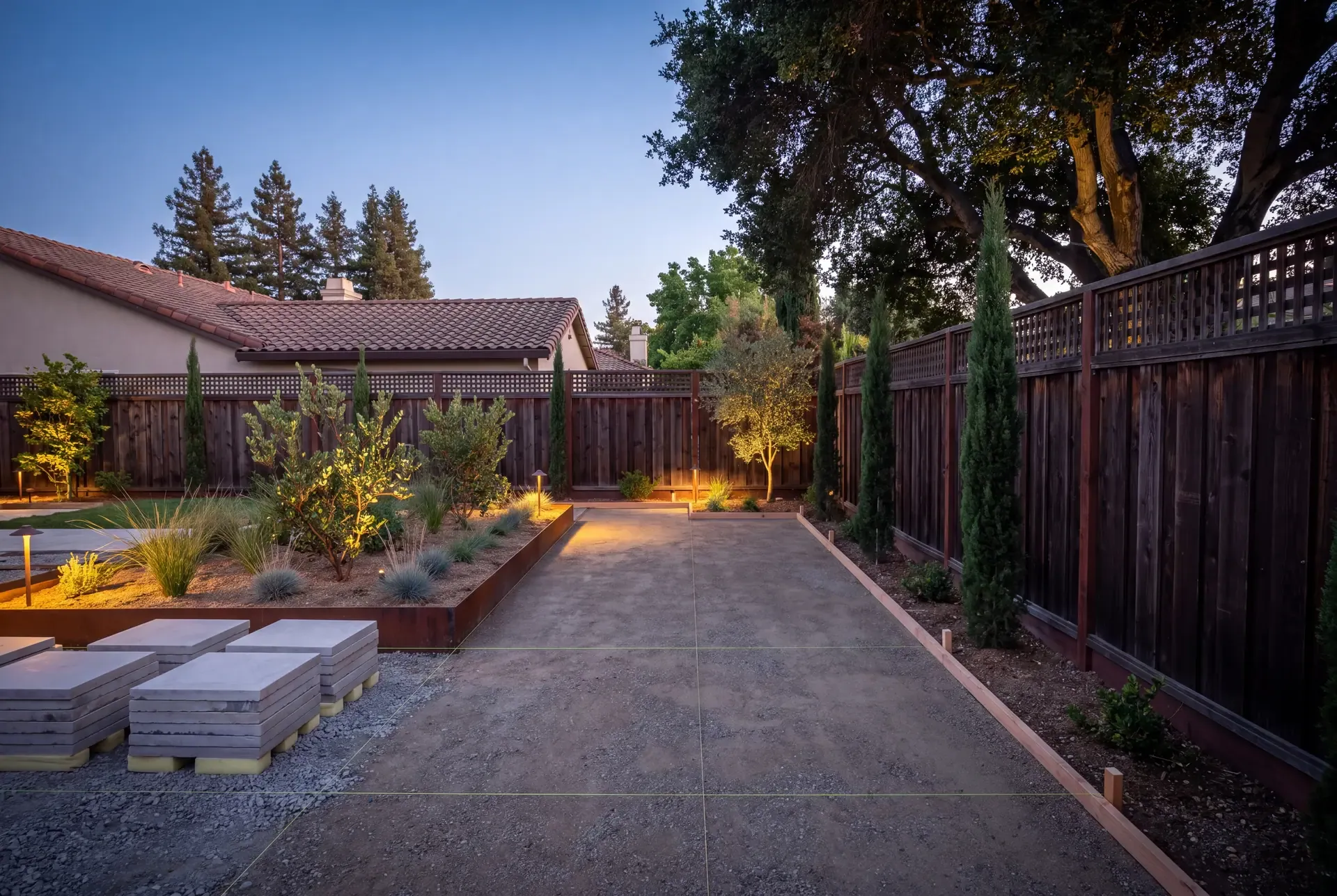 Newly completed hardscape showing compacted gravel subbase, string lines marking property boundaries, and stacked paver materials ready for installation