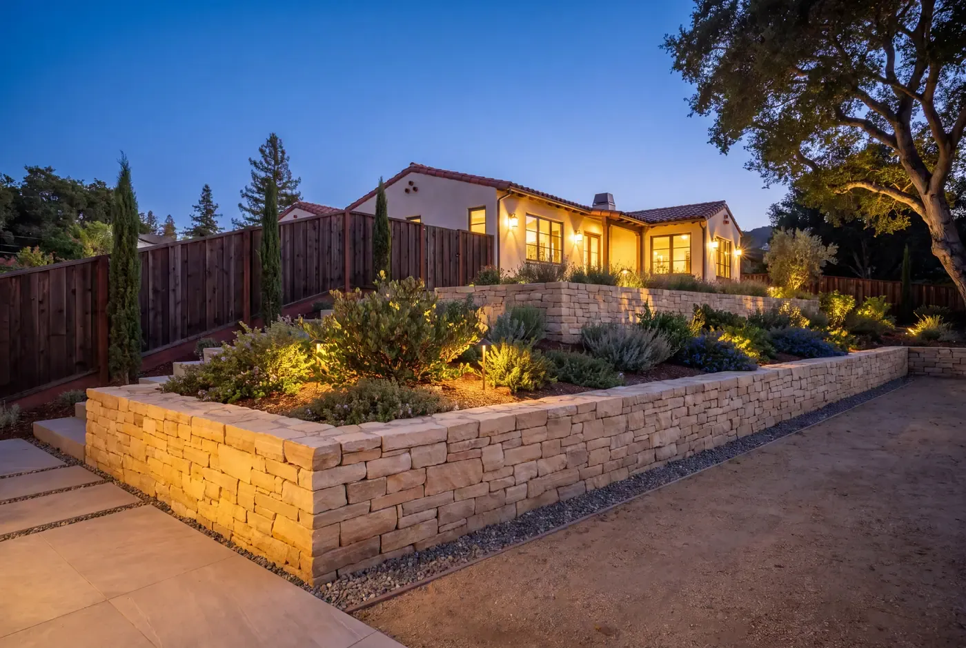 A finished hillside backyard with two low stacked-stone retaining walls, planting terraces, and a gravel drainage strip
