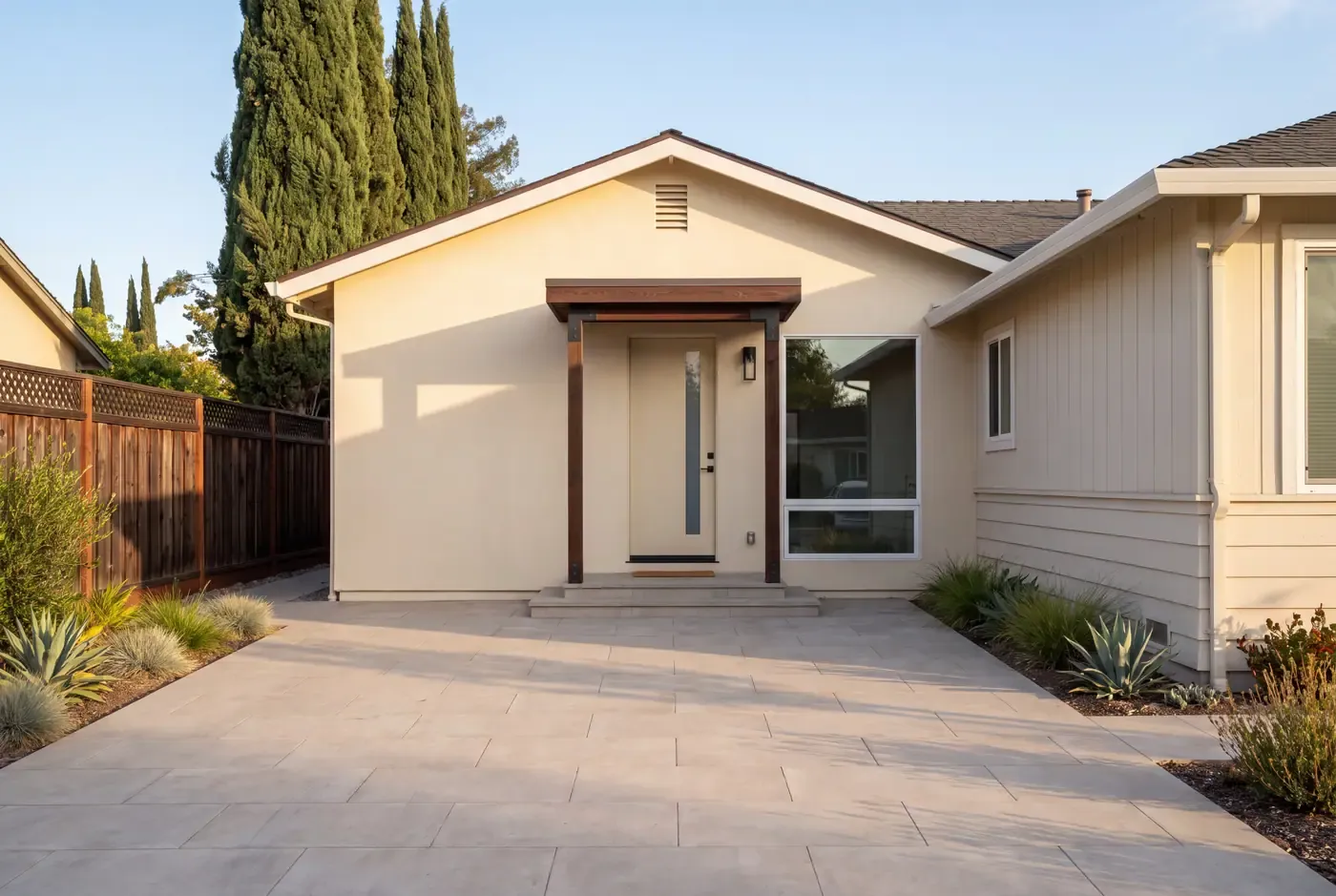 A finished garage-conversion ADU with a new entry door and fixed window, large-format porcelain pavers replacing the former driveway