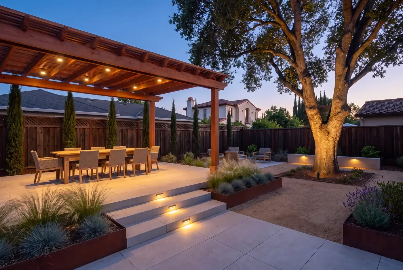 A backyard at dusk with pergola downlights on a dining table, recessed step lights on stone stairs, and a softly uplighted oak