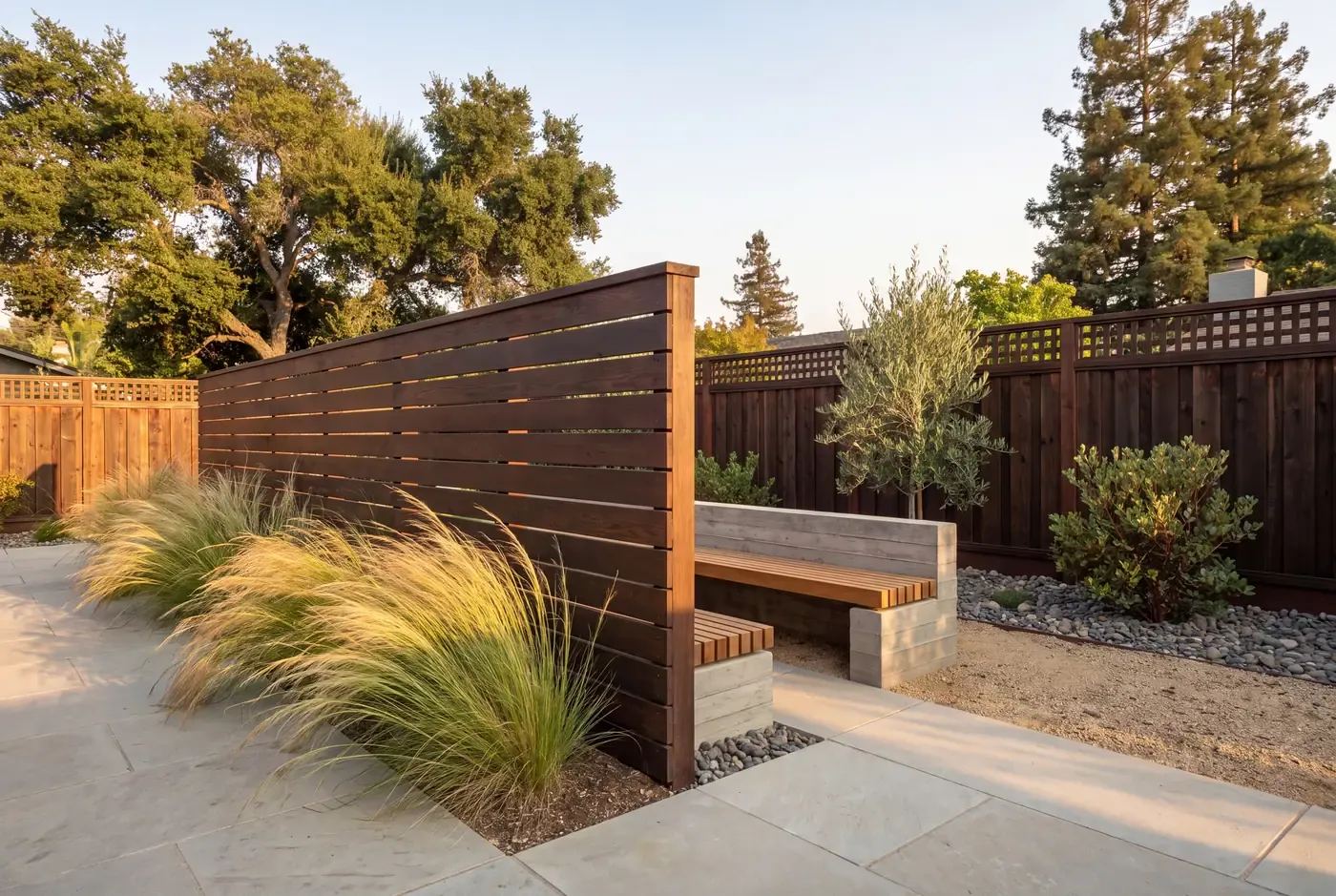 A six-foot horizontal-slat wood windbreak dividing bent grasses from a sheltered seating nook