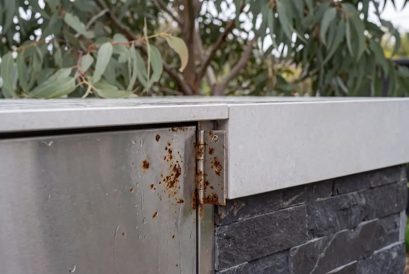 Close-up of an outdoor kitchen stainless steel door hinge showing early surface corrosion from weather exposure