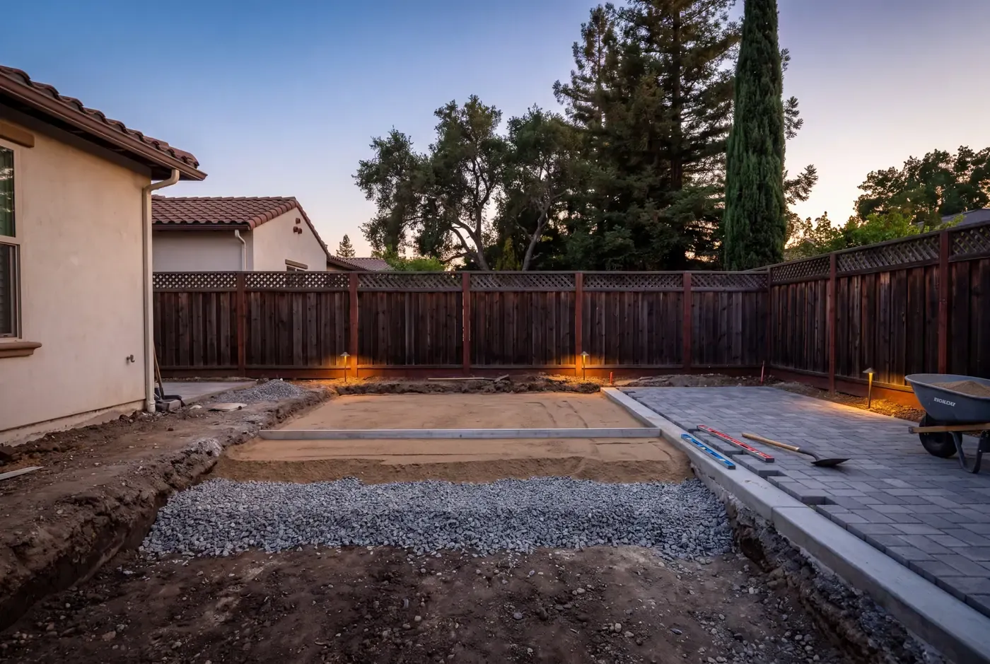 An excavated paver base in progress showing compacted subgrade, aggregate base, and bedding sand layers