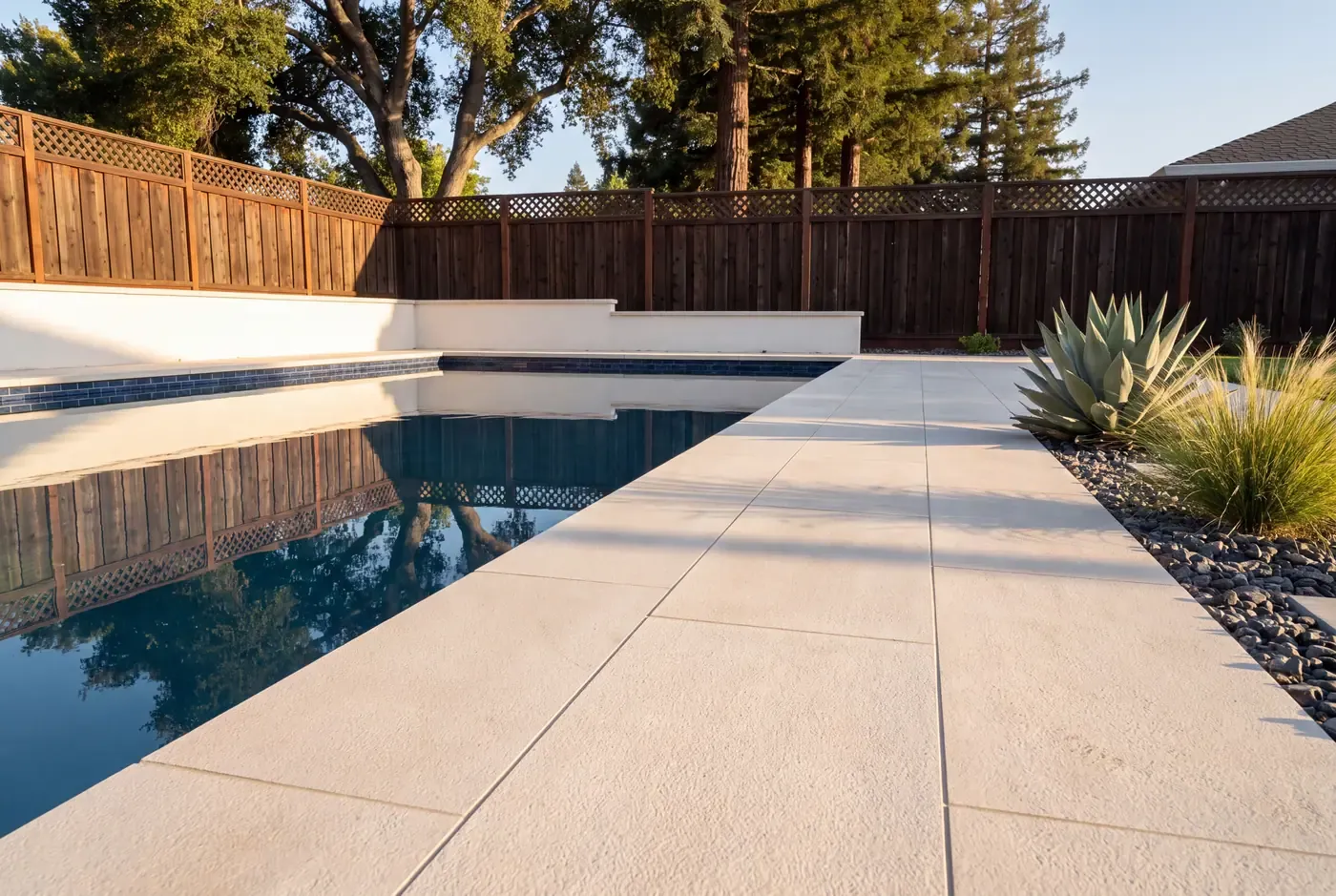 Large-format cream porcelain pavers meeting dark waterline tile at a new pool edge
